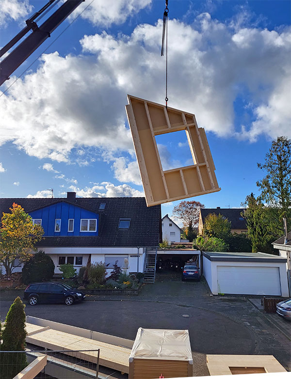 Ein fertiges Holzrahmenbauteil wird  mit dem Kran an seinen Verwendungsort gebracht