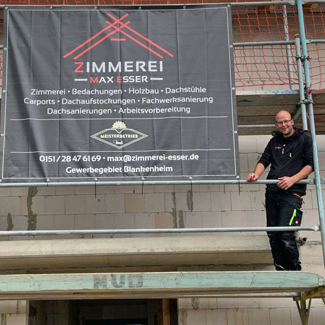 Zimmermannsmeister Max Esser steht auf einem Gerüst vor seinem Firmenbanner